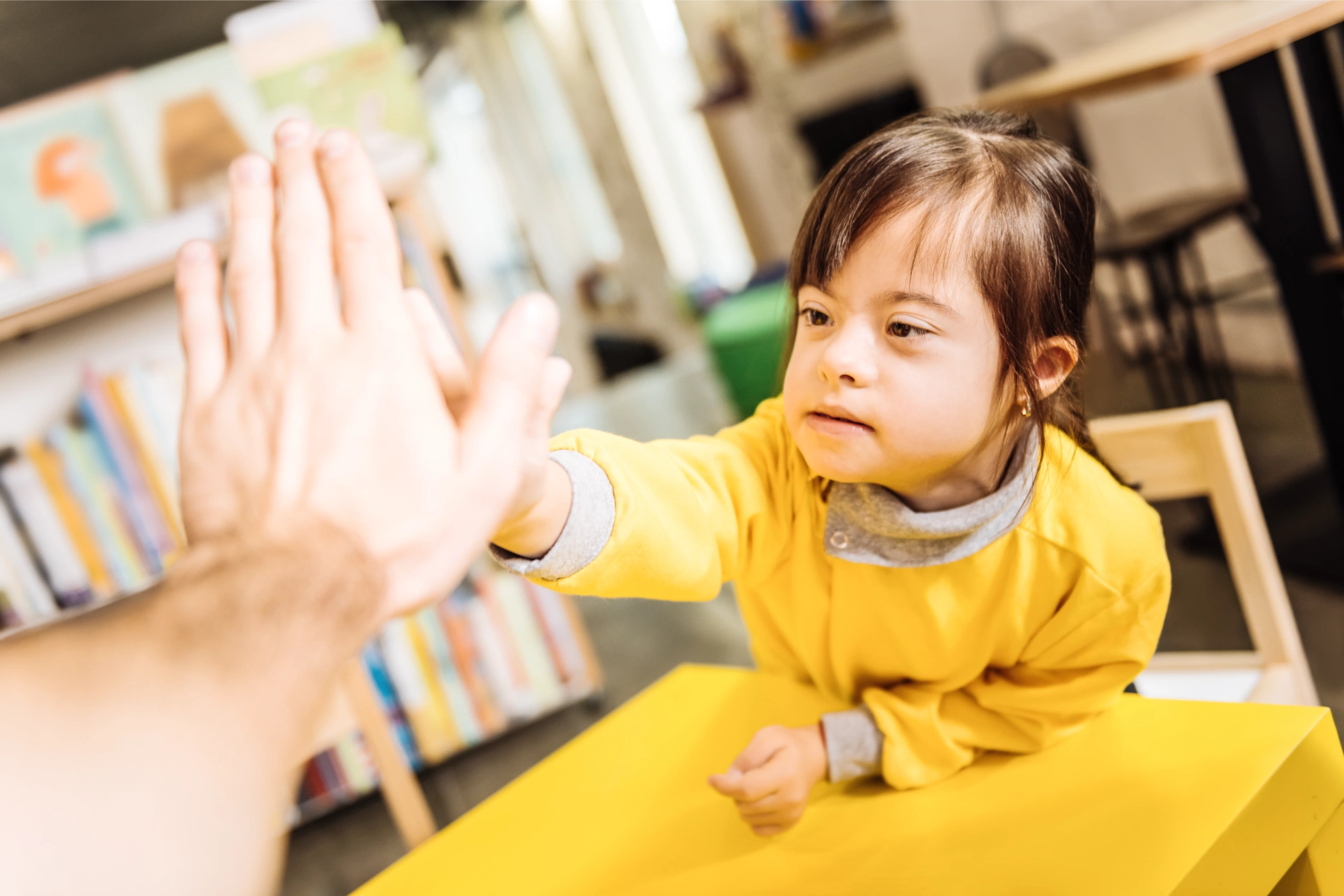 Young girl with Down syndrome giving a high-five indoors.