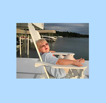 Baby relaxing in a high chair outdoors near water.