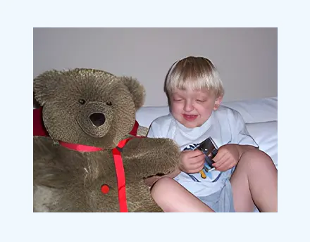 A child smiling and playing with a large teddy bear on a bed.