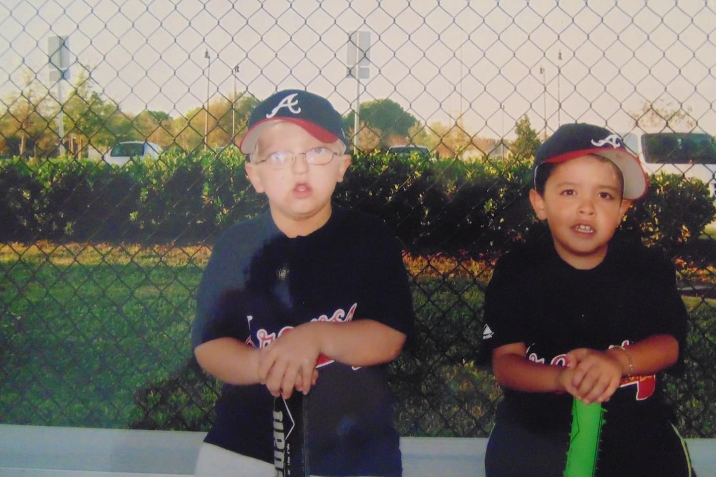 Two children wearing baseball gear posing outdoors near a fence.
