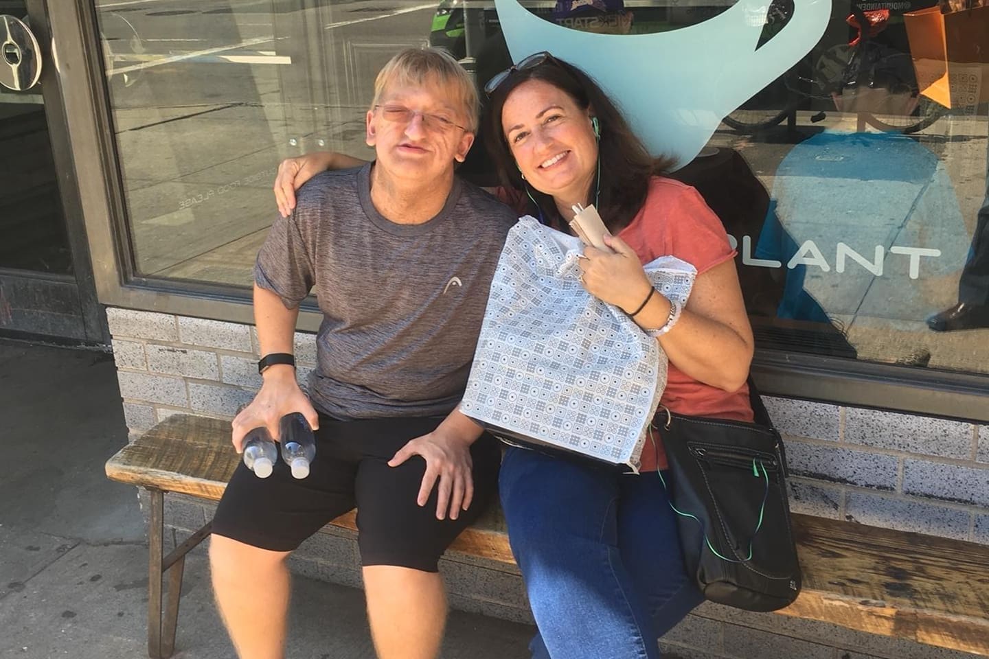 Two women smiling and holding a gift bag while sitting outdoors.