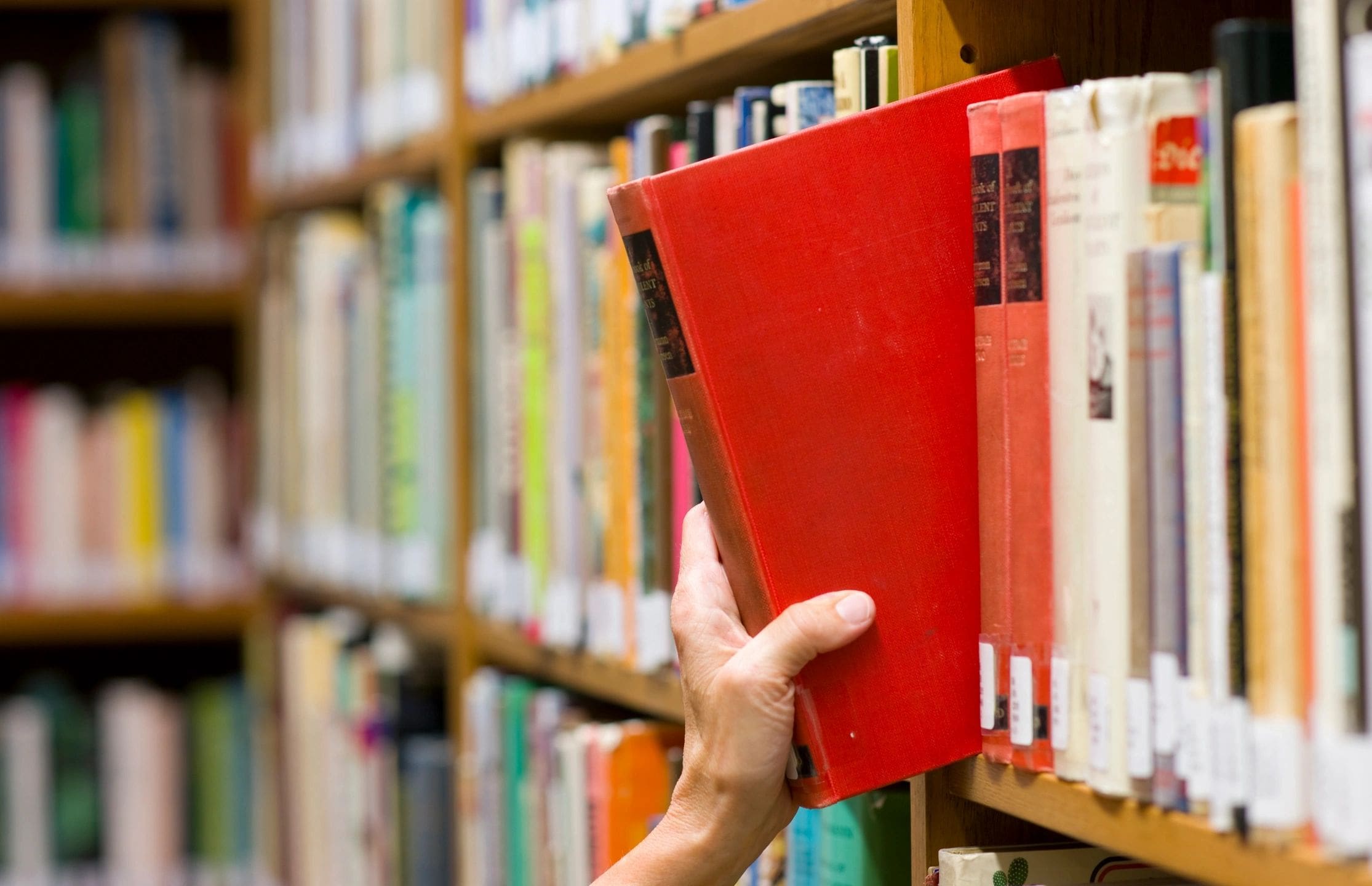 A hand pulling a red book from a library shelf.